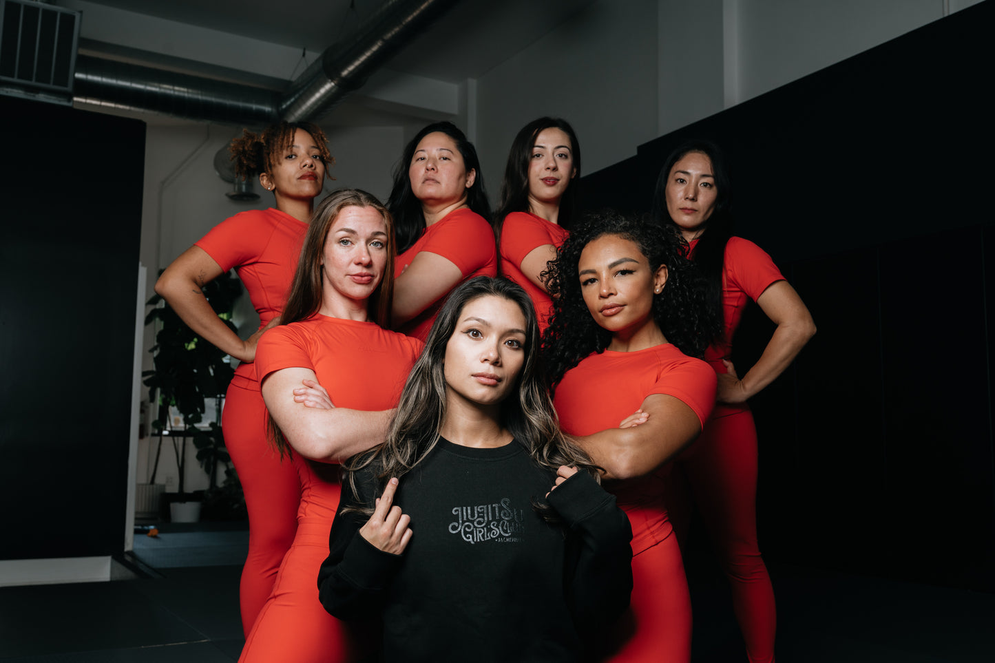 Seven women in red jiu jitsu no gi gear in a bjj gym