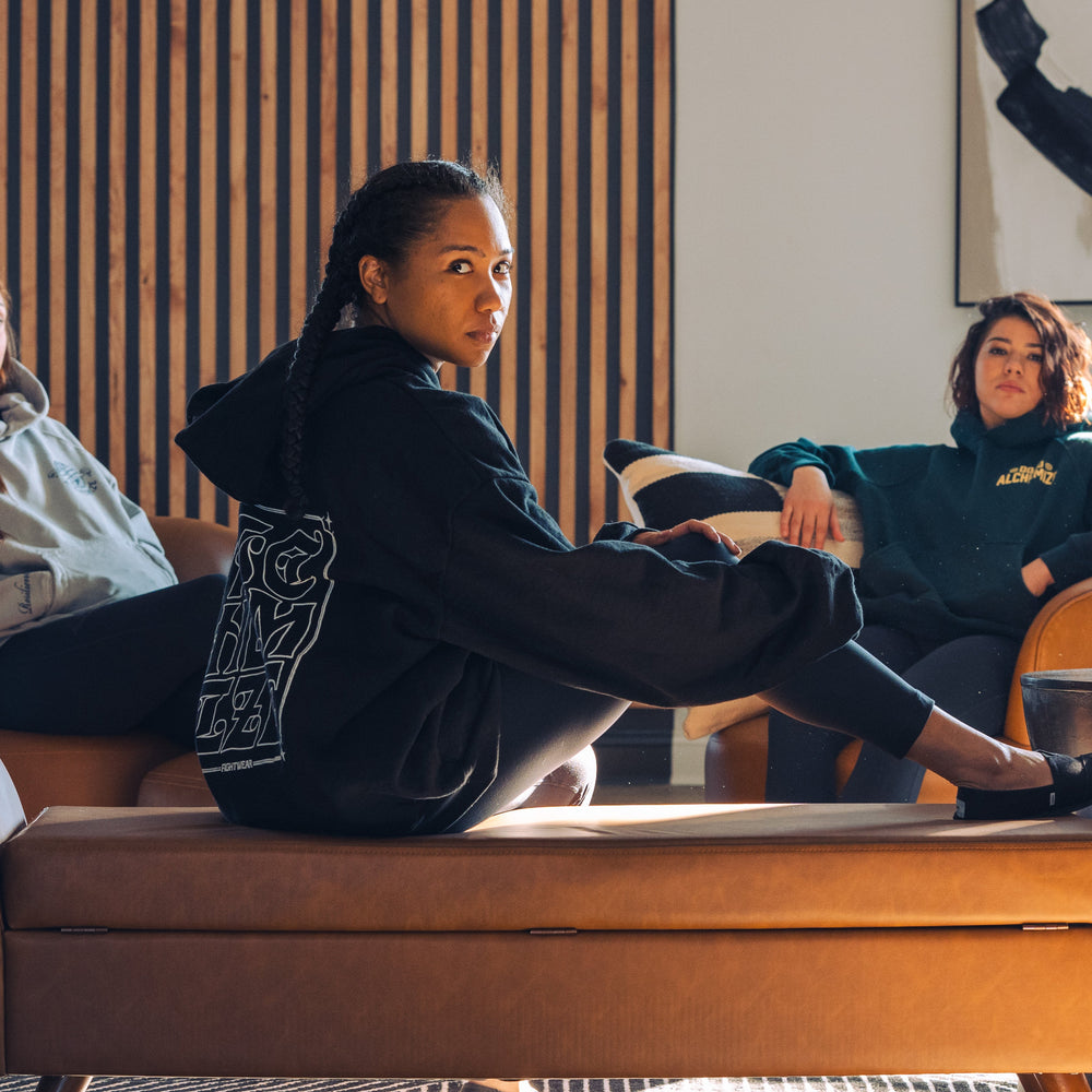 Three women sitting on chairs in sweatshirts Alchemize fightwear