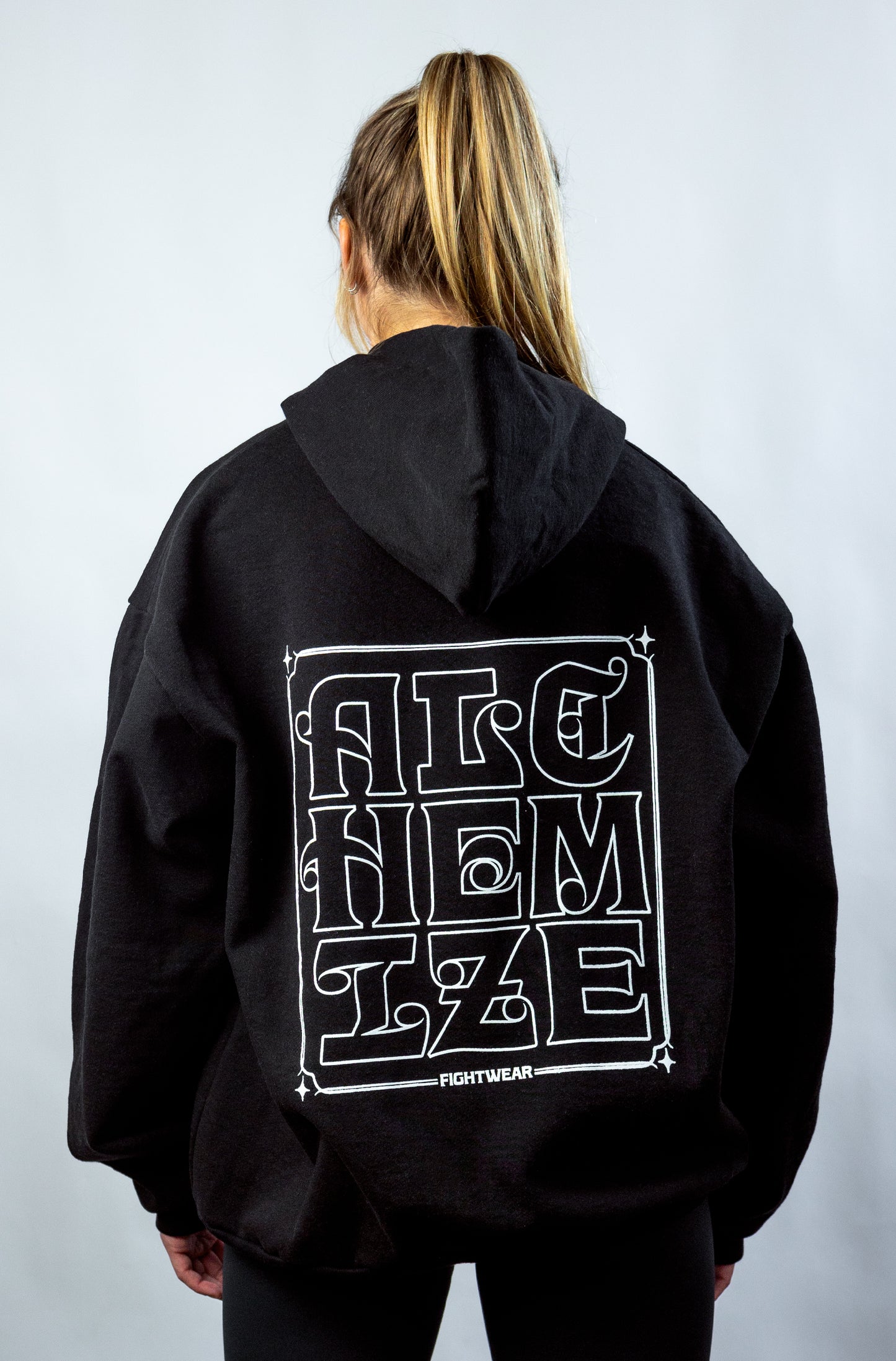 Women's black hoodie. Bold "Alchemize" pattern on back center. 